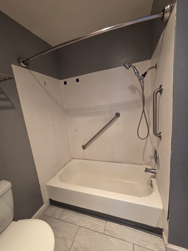 Bathtub and shower enclosure before remodel with worn fiberglass walls.