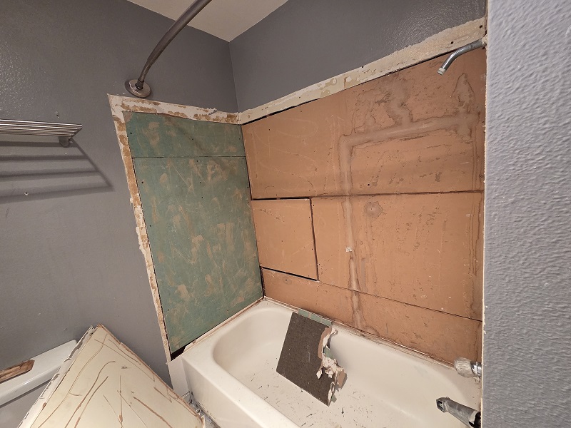 Bathroom demolition exposing wall studs, plumbing lines, and old tile removal.