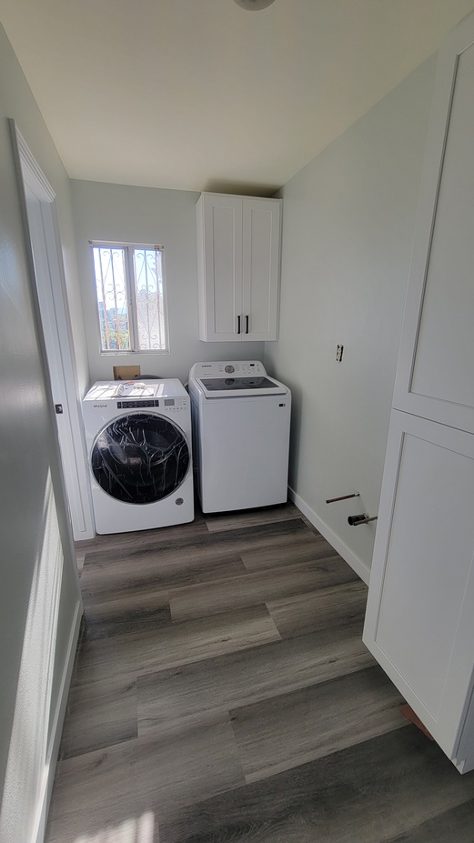 Laundry room renovation with new washer, dryer, cabinetry, and modern vinyl plank flooring.