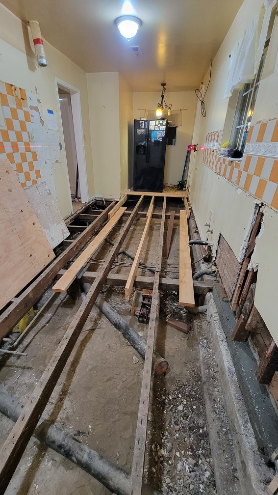 Kitchen demolition showing exposed subfloor, plumbing work, and removed cabinets.