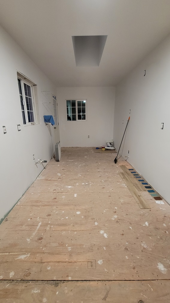 Kitchen renovation phase with drywall installed and new wood subfloor.