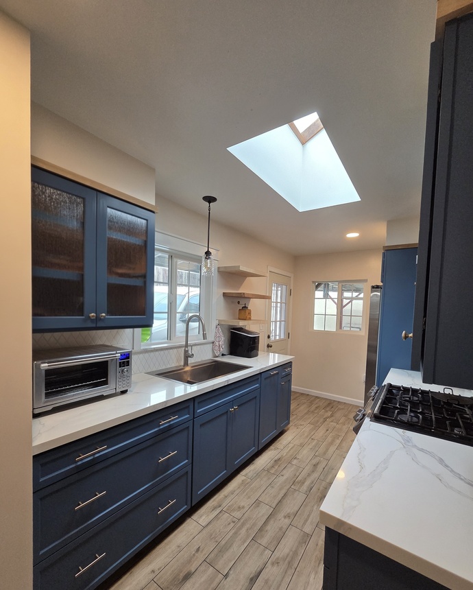 Kitchen renovation with blue shaker cabinets, quartz countertops, and skylight lighting.