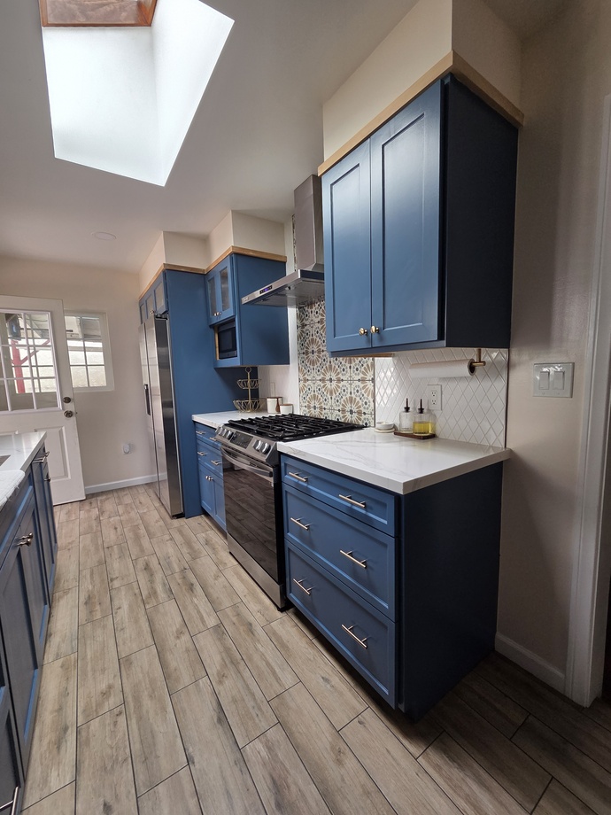Completed kitchen remodel featuring blue shaker cabinets, tile backsplash, and stainless appliances.