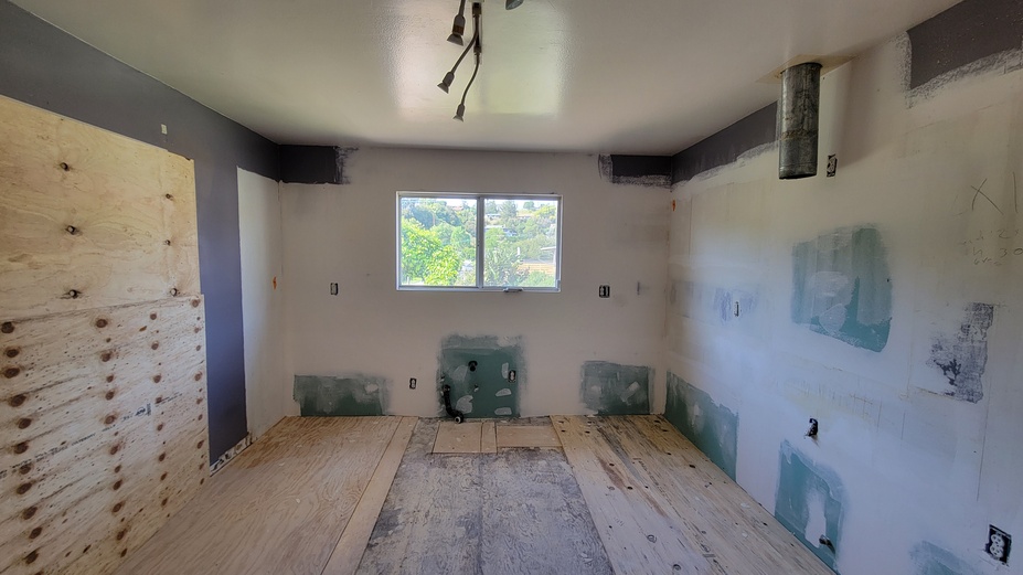 Kitchen demolition stage showing exposed wall plumbing and electrical work.