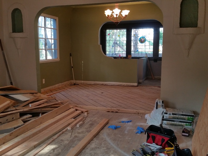 Living room demolition during home remodel with flooring removed and framing exposed.